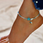 Charger l'image dans la galerie, A close-up image of a foot wearing a white and turquoise beaded ankle bracelet with a starfish charm.
