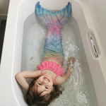 Load image into Gallery viewer, A young girl lying in a white bathtub wearing a mermaid tail swimsuit with a pink ruffled top and a blue, pink, and green gradient mermaid tail.