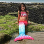 Load image into Gallery viewer, Girl sitting on the beach with her Pink & Blue Mermaid Tail with matching material embellished bow halterneck bikini.