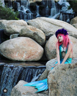 Load image into Gallery viewer, Sweet little girl mermaid with red hair and purple flowers on her head sitting on rocks by a waterfall and wearing the Ocean Blue double frill bikini with matching vibrant mermaid tail. Part of our luxury range, this tail has a high quality side zip. Mini Mermaid Tails