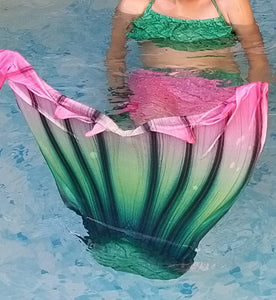 Girl in pool wearing the Pretty Green & Pink Mermaid Tail with added dorsal fins. Reminiscent of a watermelon. Complete with matching, larger, more coverage, frill halter-neck bikini. Part of our luxury range, this tail has a high quality side zip. Mini Mermaid Tails