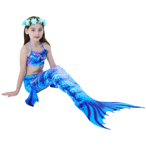 Smiling girl wearing a Bold Blue Tiger Mermaid Tail with just a splash of purple. Complete with dorsal fins for a true little mermaid look and matching material halterneck bikini with cute embellished bow and blue flowers in her hair. Mini Mermaid Tails