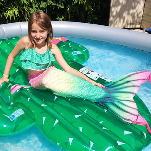 Smiling girl on a cactus float in a swimming pool wearing the Pretty Green & Pink Mermaid Tail with added dorsal fins. Reminiscent of a watermelon. Complete with matching, larger - more coverage, frill halterneck bikini. Part of our luxury range, this tail has a high quality side zip. Mini Mermaid Tails