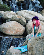 Load image into Gallery viewer, Sweet little girl mermaid with red hair and purple flowers on her head sitting on rocks by a waterfall and wearing the Ocean Blue double frill bikini with matching vibrant mermaid tail. Part of our luxury range, this tail has a high quality side zip. Mini Mermaid Tails
